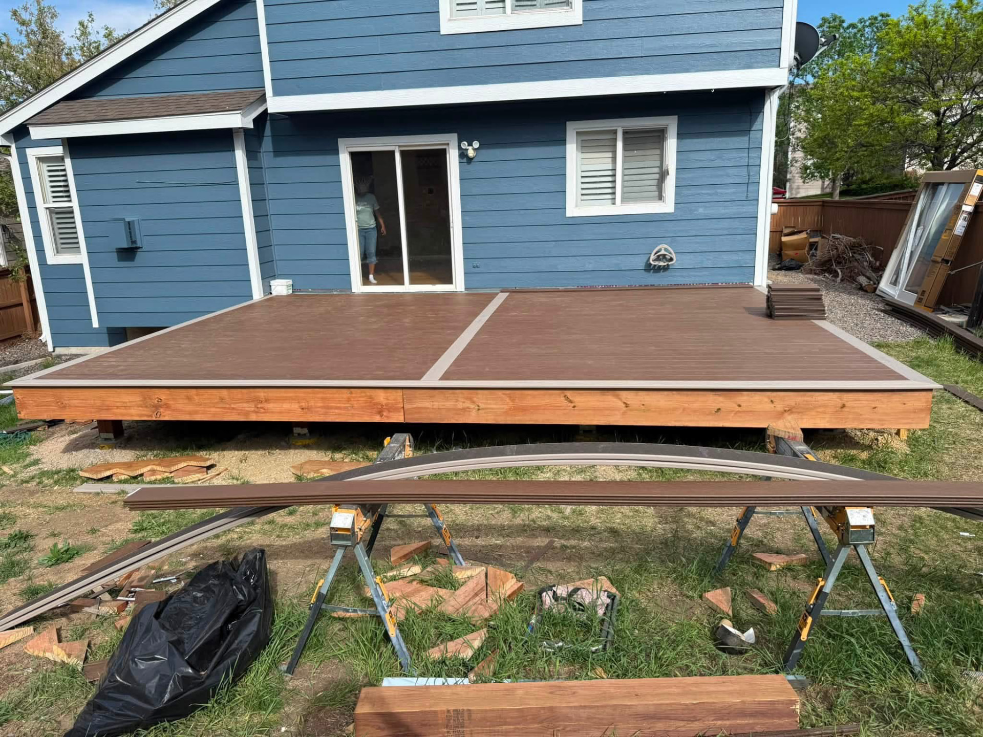 Ground-level deck under construction beside a blue-sided home