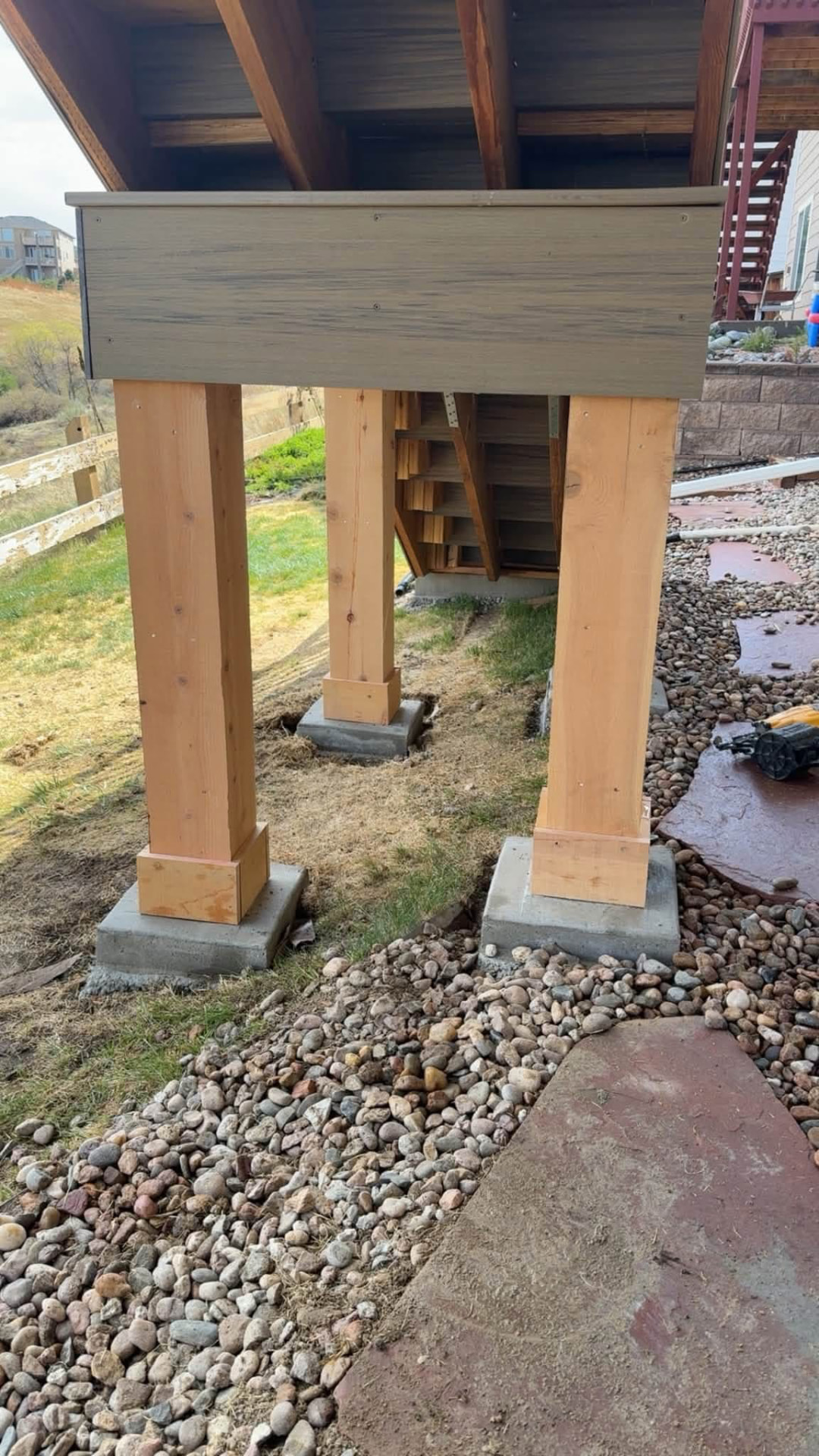 Wood support posts on concrete footings beneath a deck staircase