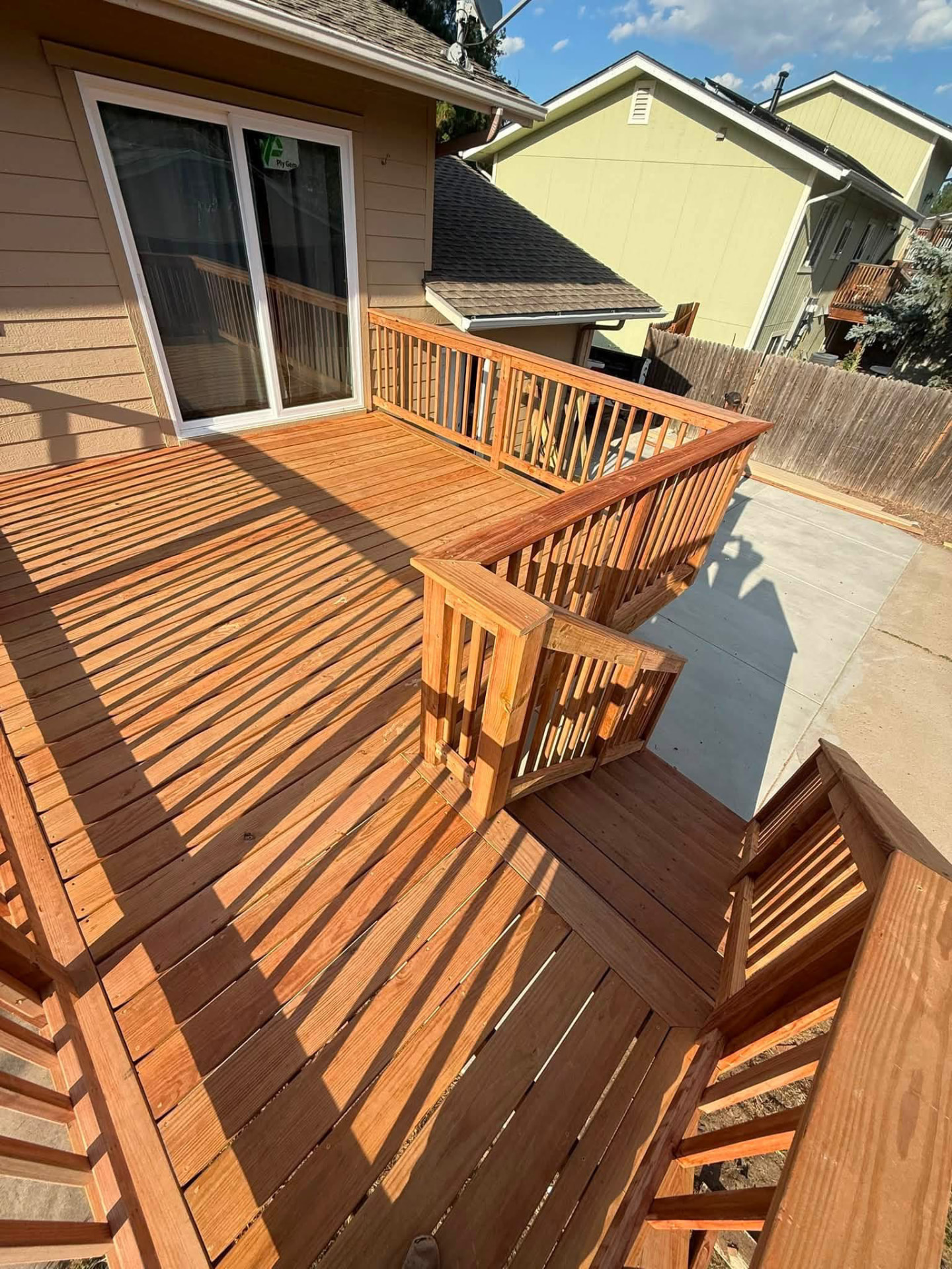 Stained wood deck with railings and stairs leading down to a concrete patio
